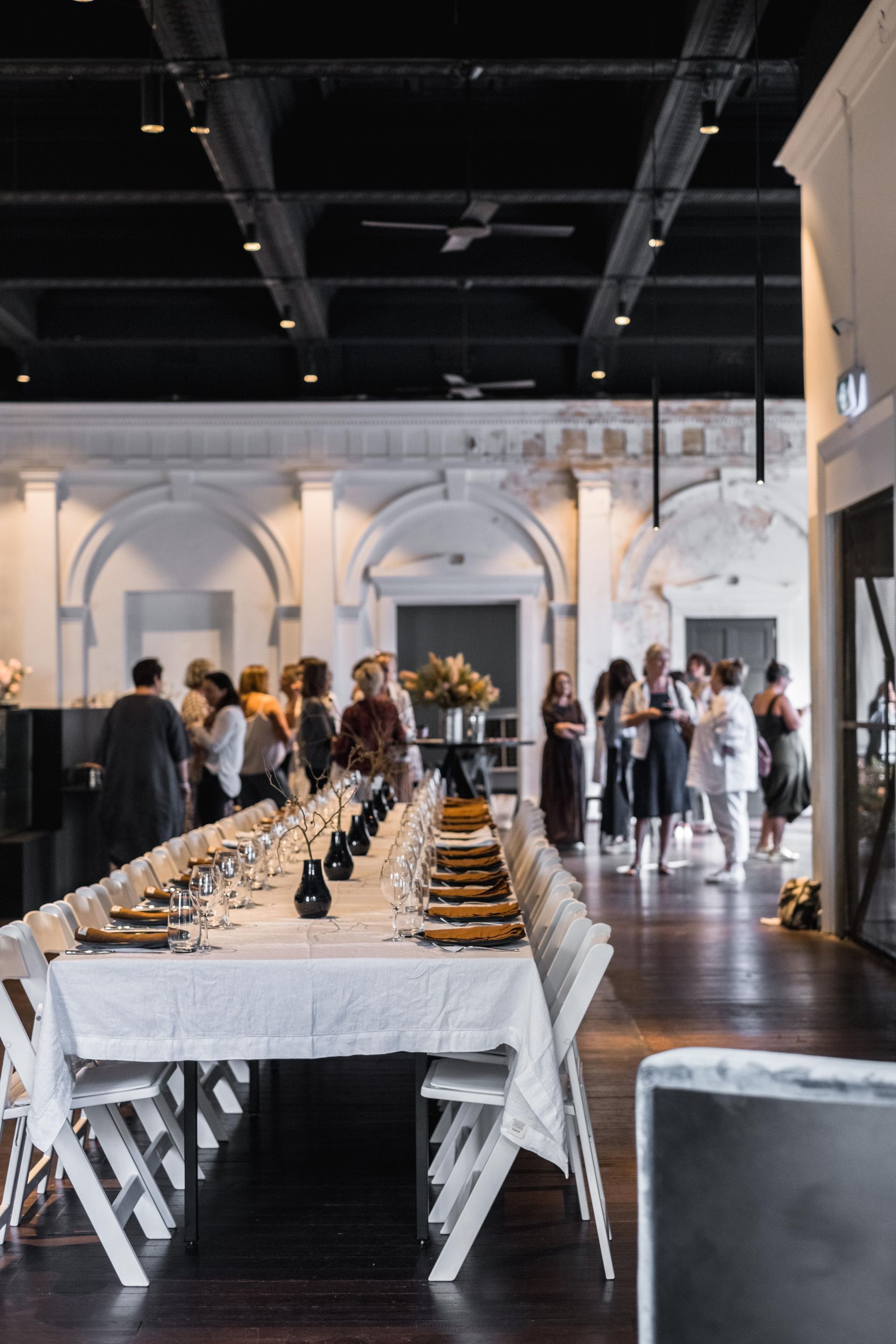 Long banquet table set in a bright hall with guests mingling in the background