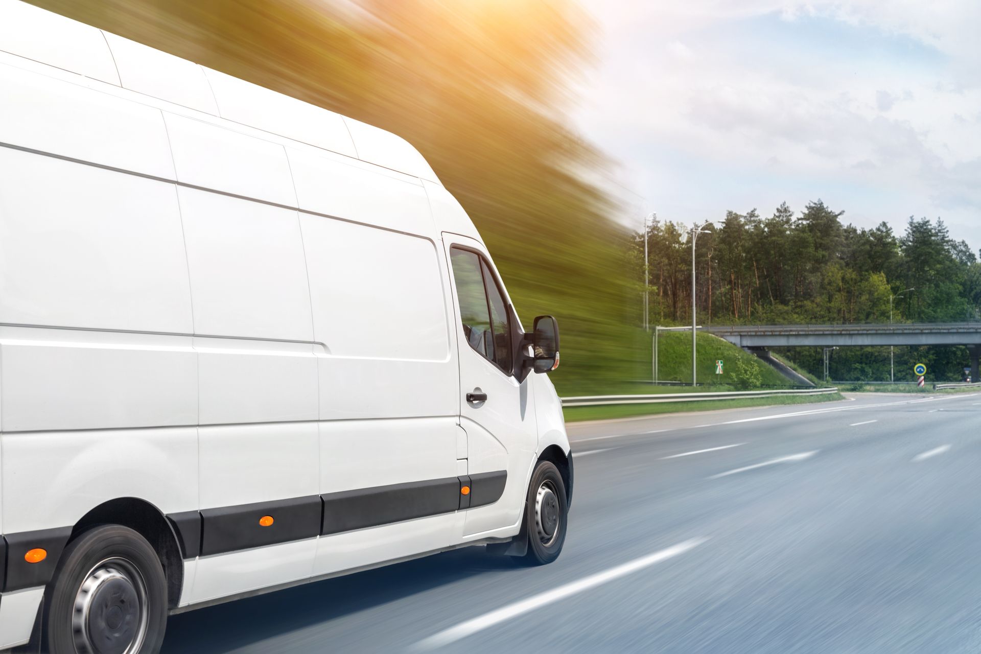 White delivery van driving on a highway with motion blur and trees along the roadside