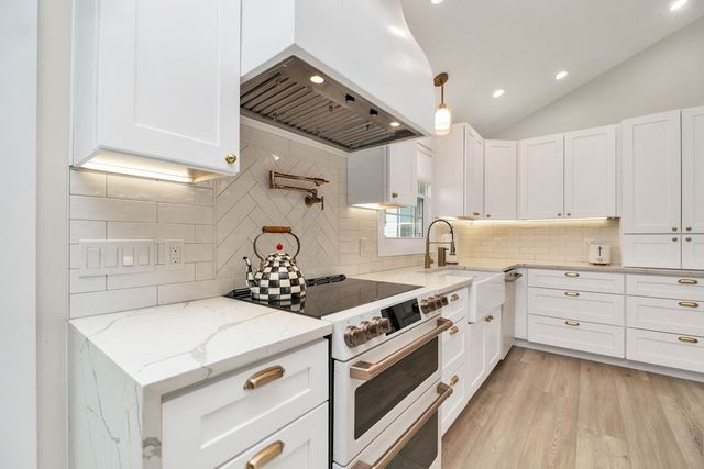 Bright white modern kitchen with stainless steel stove, subway tile backsplash, and wood floors