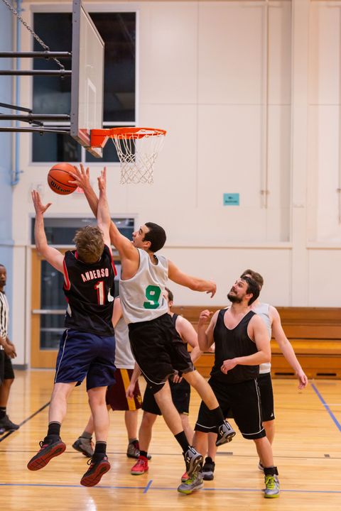 Basketball players contest a shot near the hoop in an indoor gym