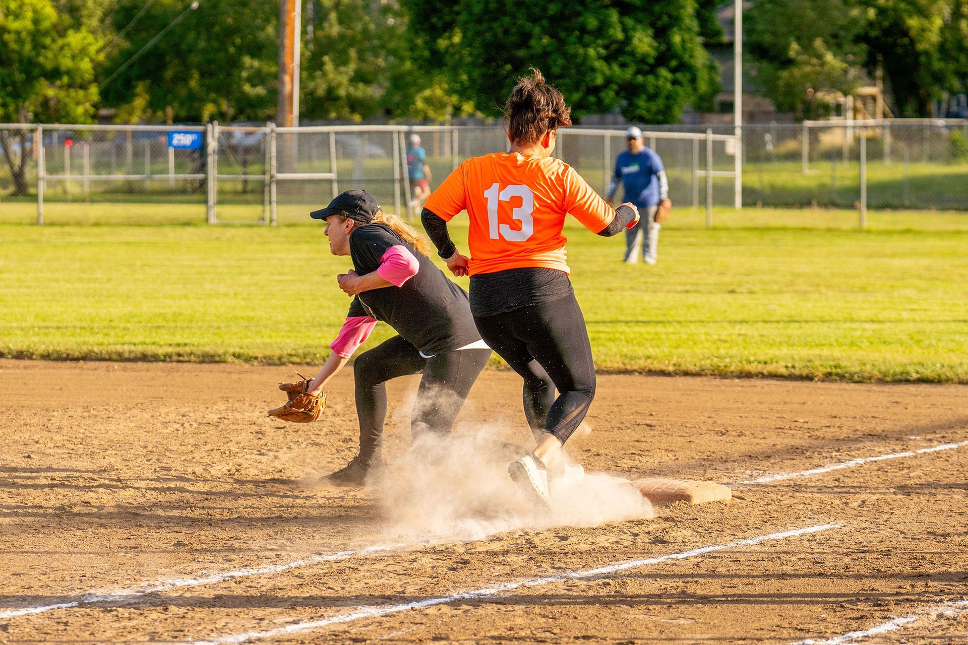 Softball players collide near home plate as one slides in, kicking up dust on a sunny field