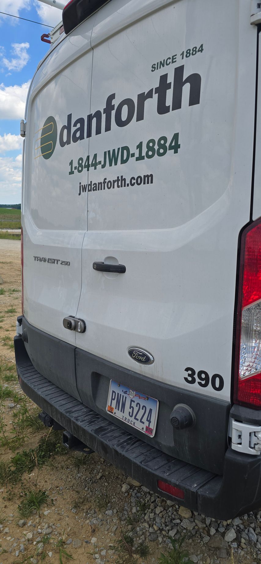 White work van with company logo and phone number, parked outdoors near grass.