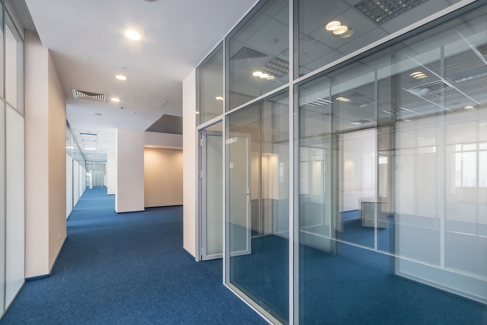 Empty office hallway with blue carpet and glass-walled rooms
