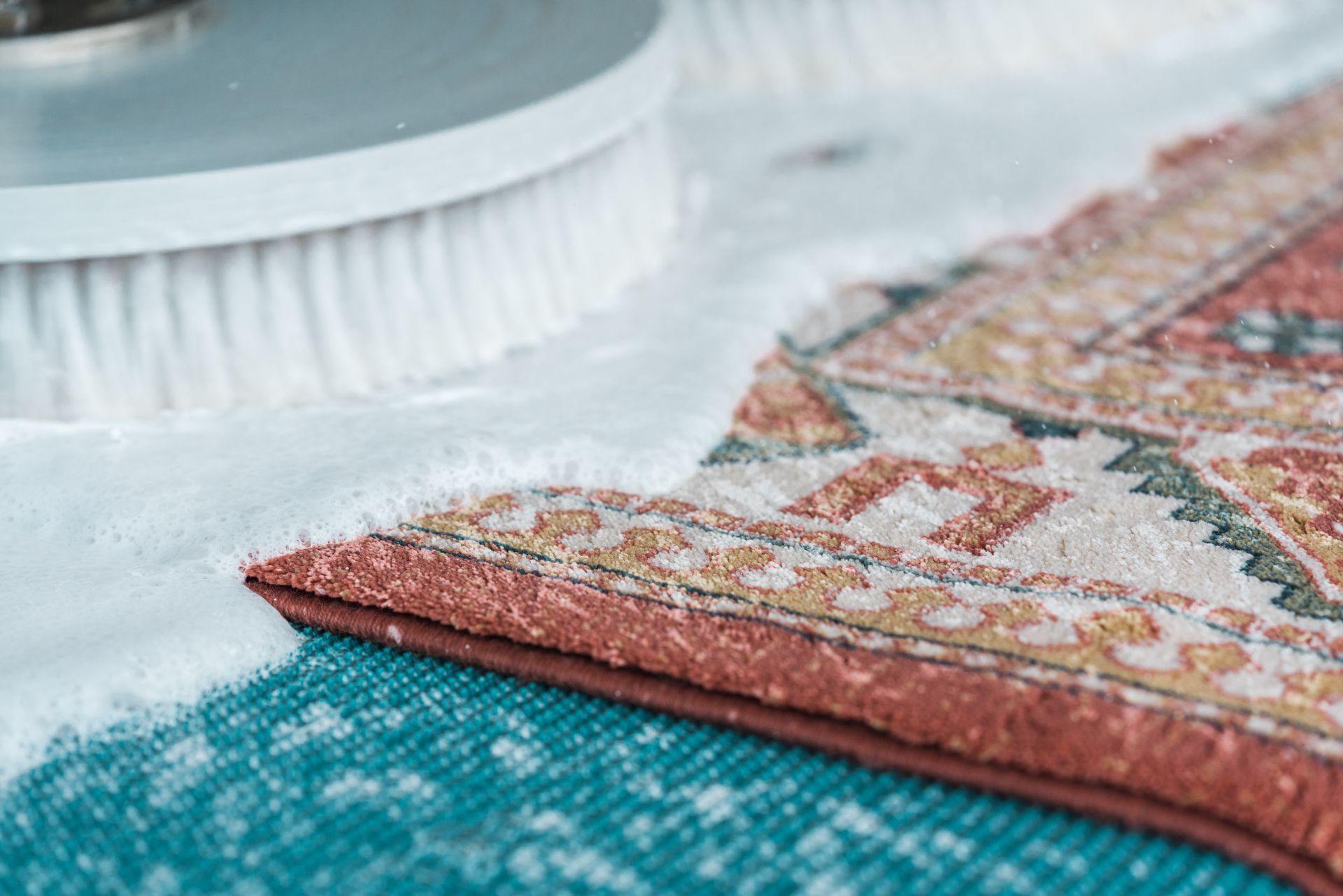 Folded patterned rug on a blue carpet beside a white brush and a woven basket edge