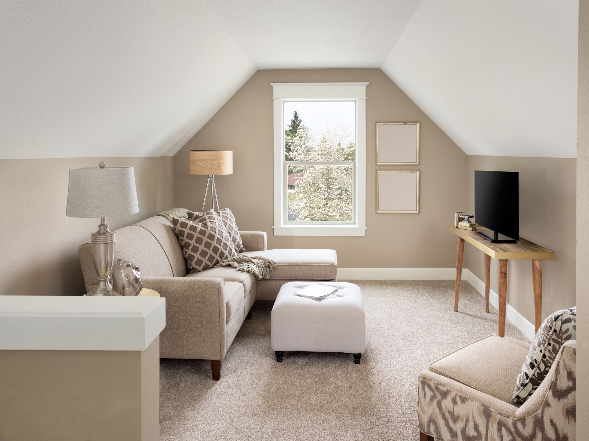 Cozy beige attic living room with sectional sofa, ottoman, lamp, and TV on a wooden table