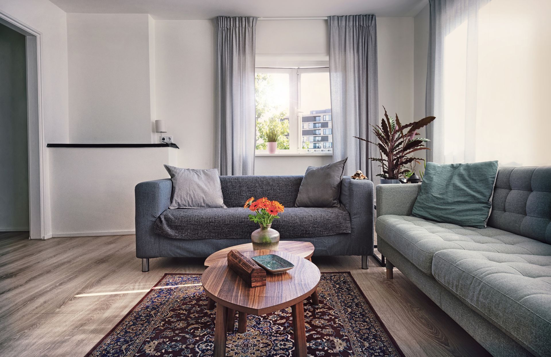 Modern living room with gray sofas, round coffee table, rug, and a window with curtains