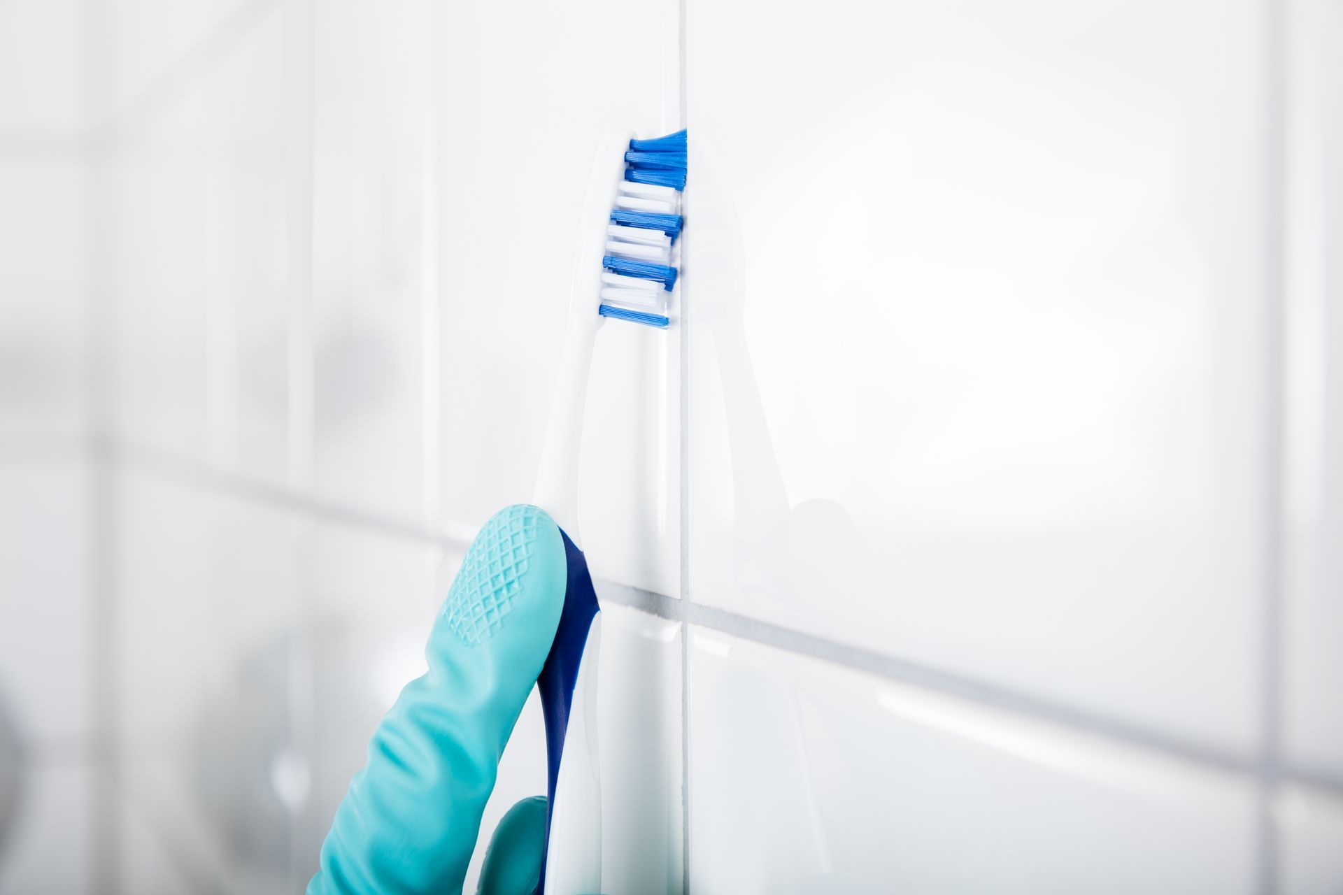 Gloved hand holding a toothbrush against white bathroom tiles