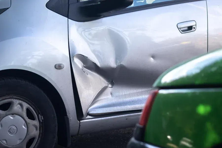 Silver car with a large dent on the front door with unfortunate paint damage.