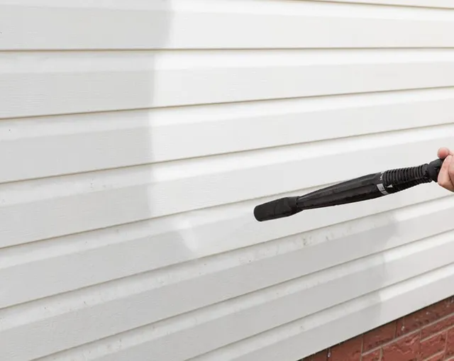 A Person Uses a Power Washer on White Vinyl Siding — MDSR Group In Manunda, QLD