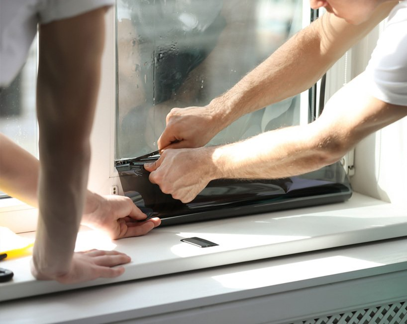 Two People Installing Window Tint Film on a Window in a White-walled Room — MDSR Group In Manunda, QLD