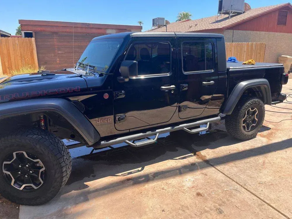 A black jeep gladiator pickup truck is parked in a driveway.