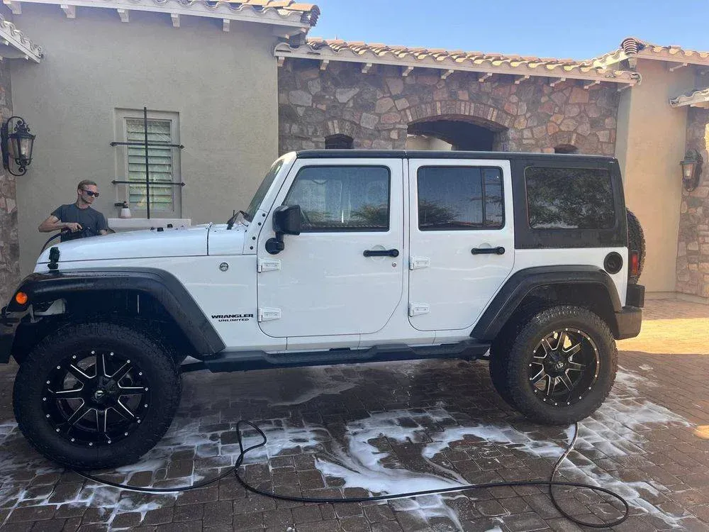 A white jeep is being washed in front of a house.