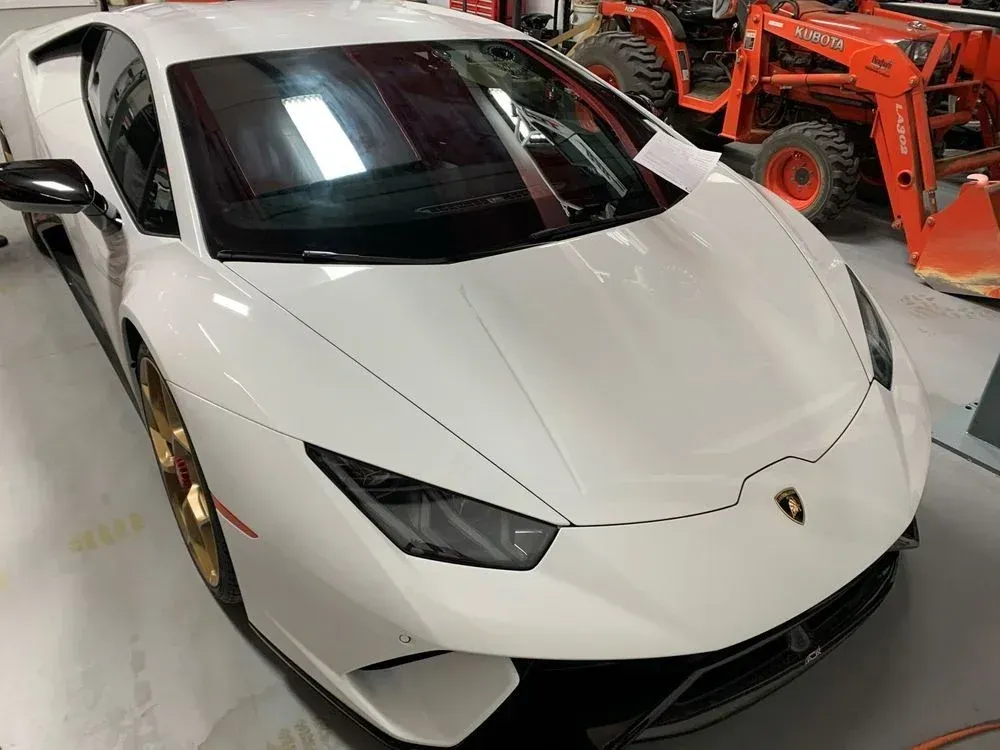 A white lamborghini huracan is parked in a garage next to a tractor.