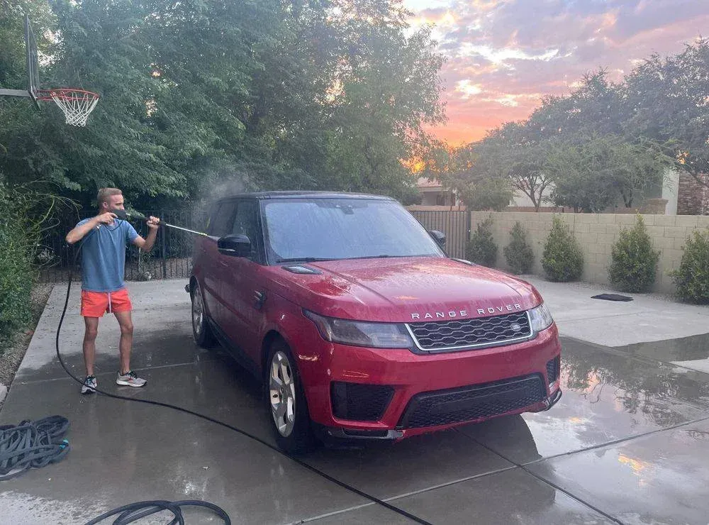 A man is washing a red range rover sport in a driveway.