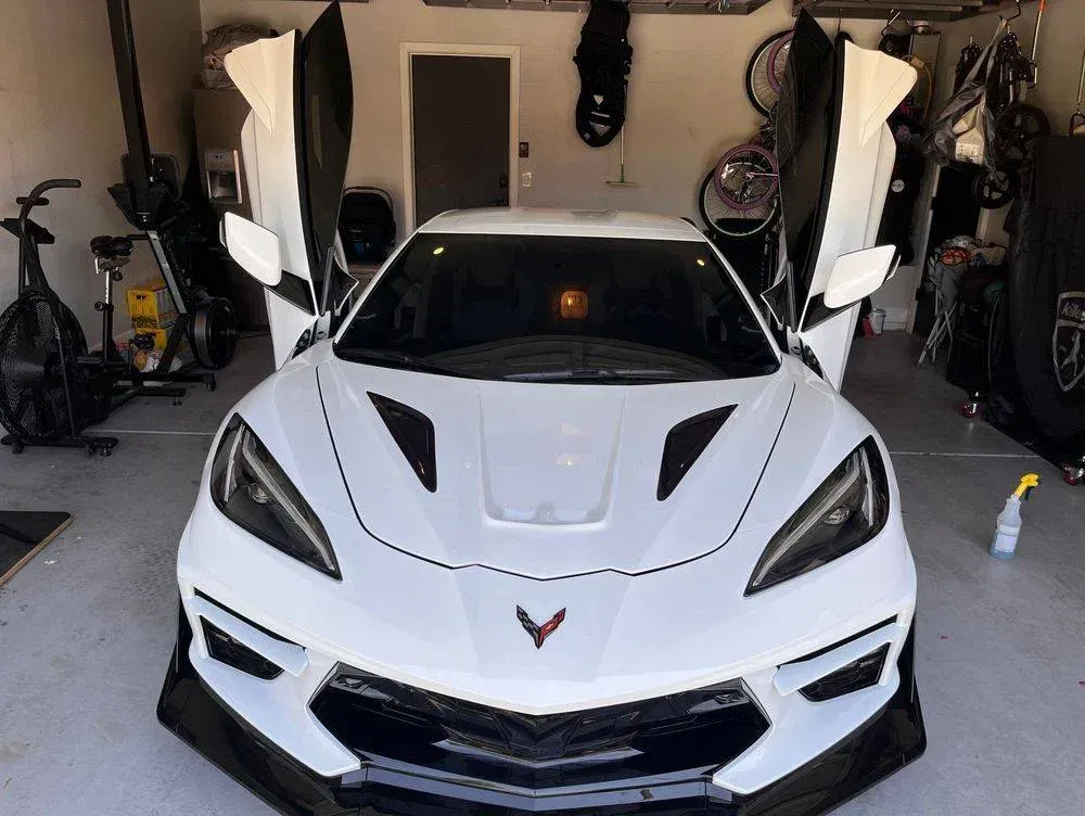 A white sports car is parked in a garage with its doors open.