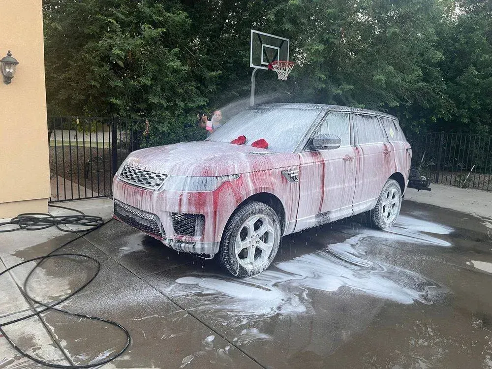 A car is covered in foam in a driveway next to a basketball hoop.
