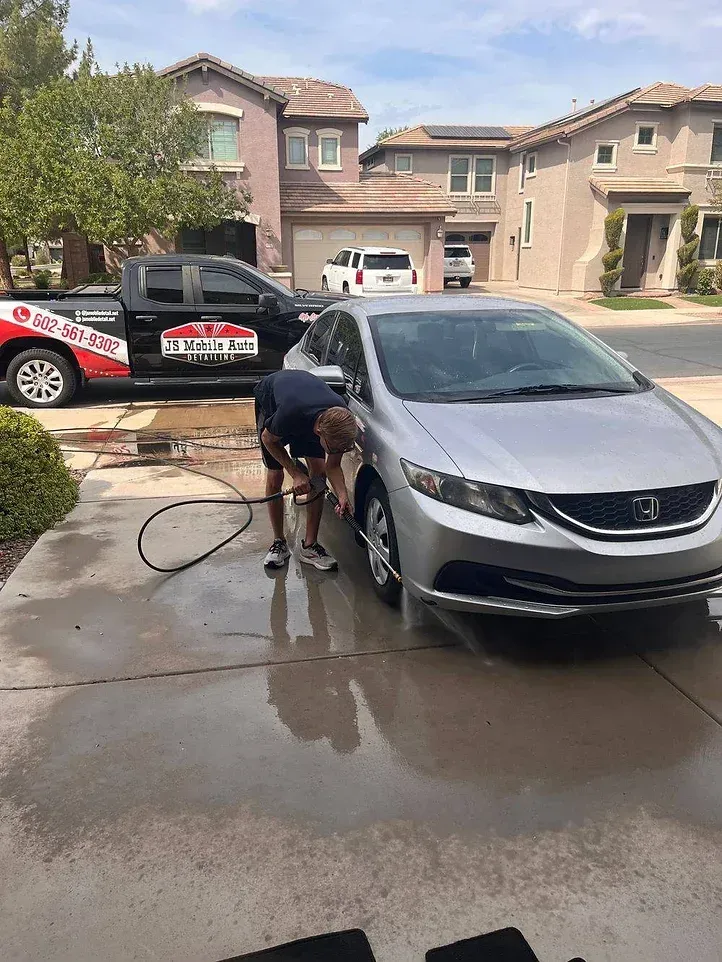 A man is washing a silver car in a driveway.