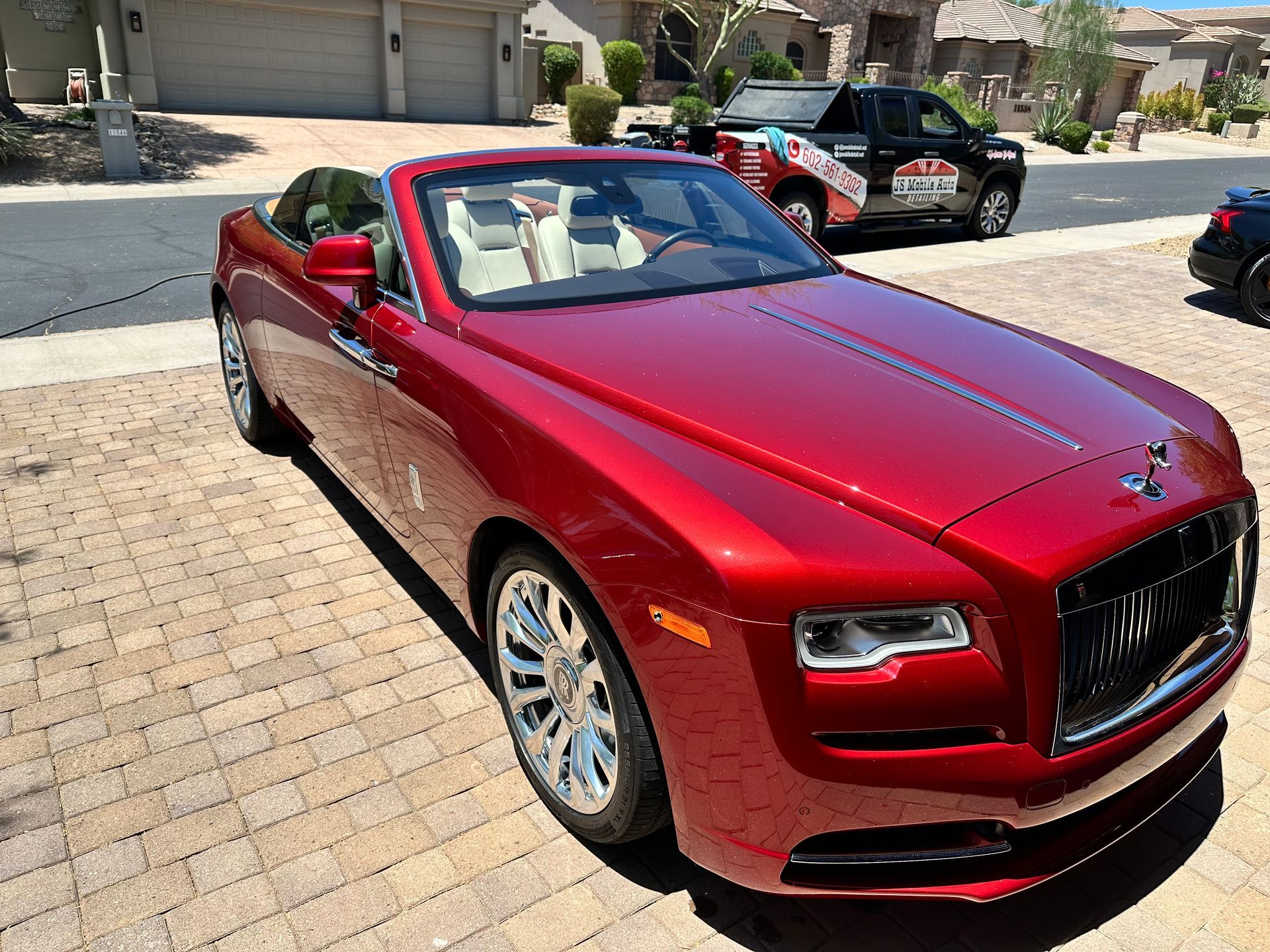 A red rolls royce convertible is parked in front of a garage.