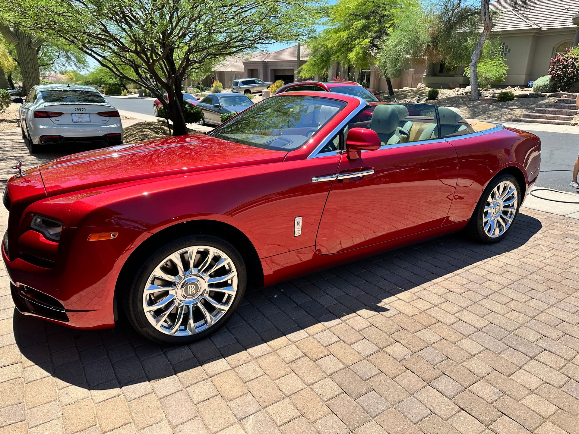 A red rolls royce convertible is parked on a brick driveway.