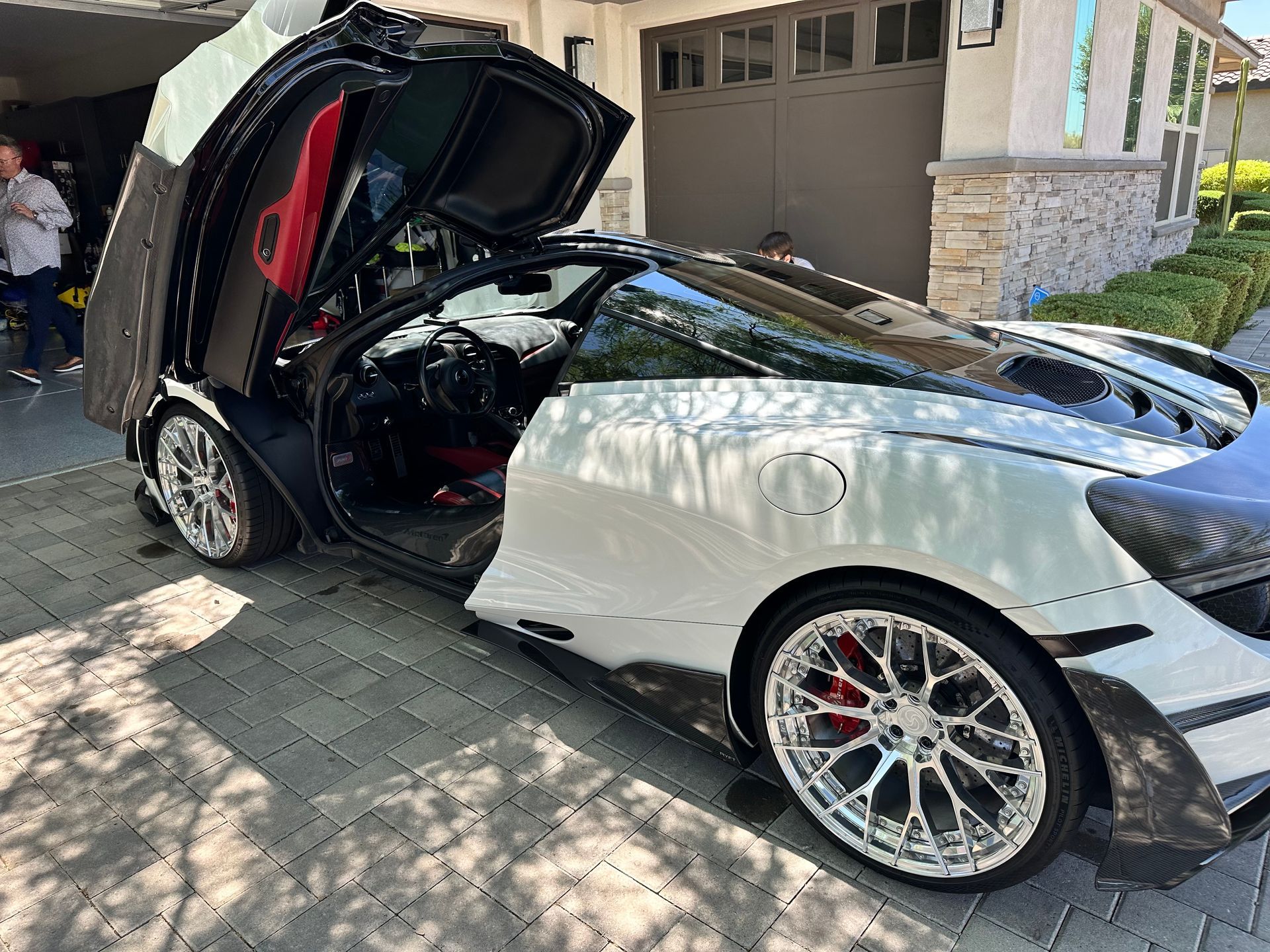 A white sports car with the hood open is parked in front of a garage.