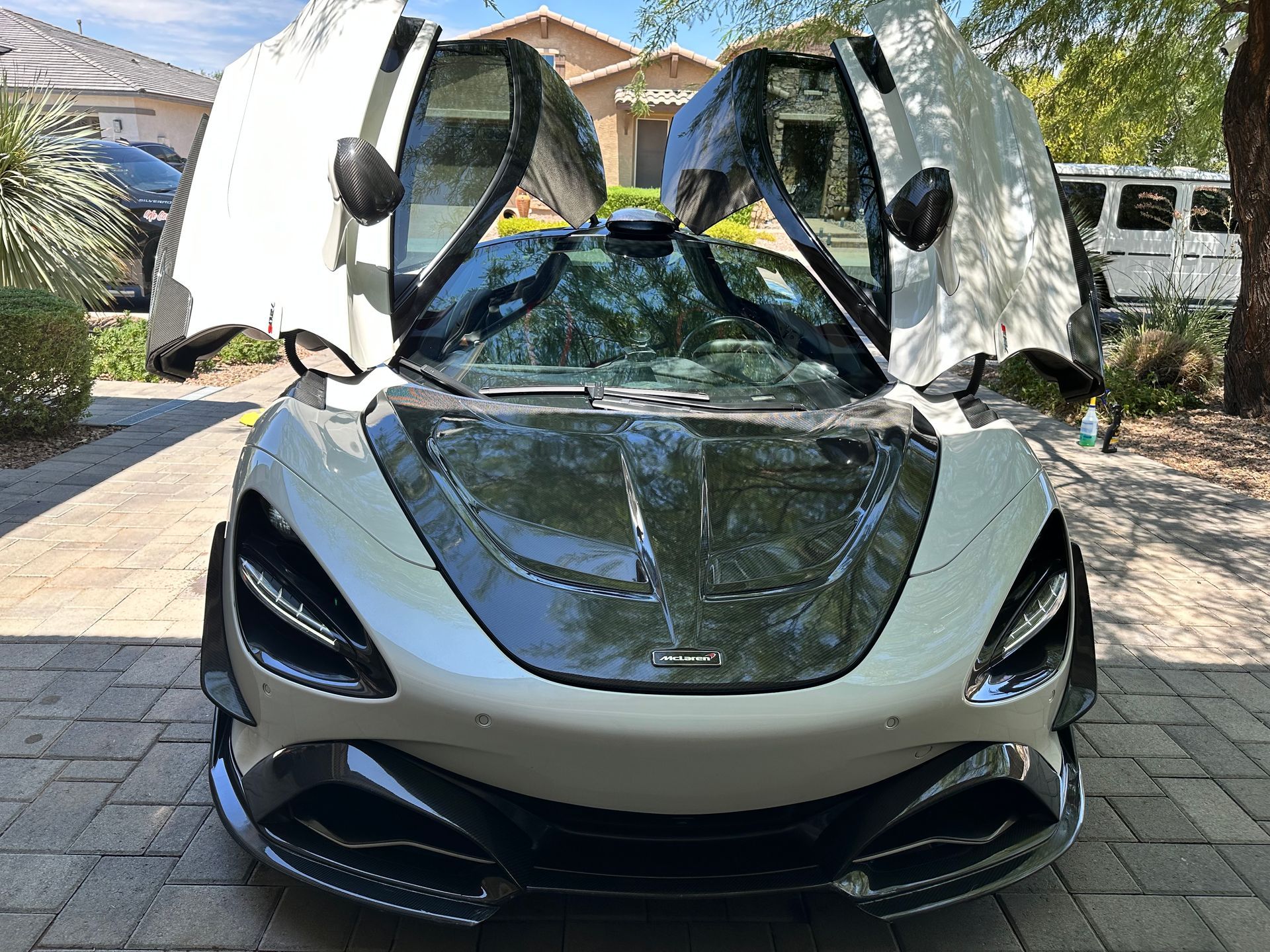 A white sports car is parked in a driveway with its doors open.