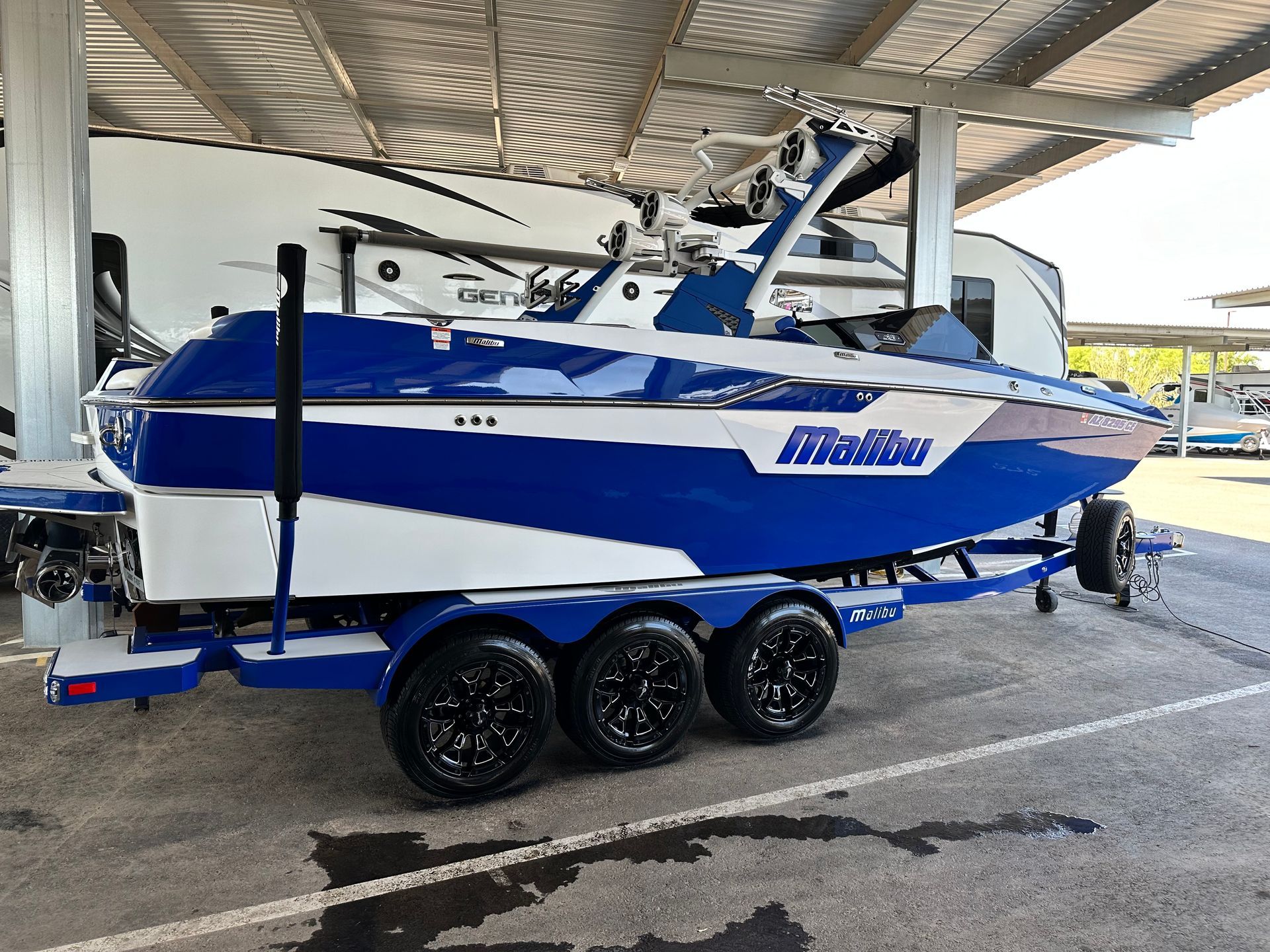 A blue and white boat is parked under a roof in a parking lot.