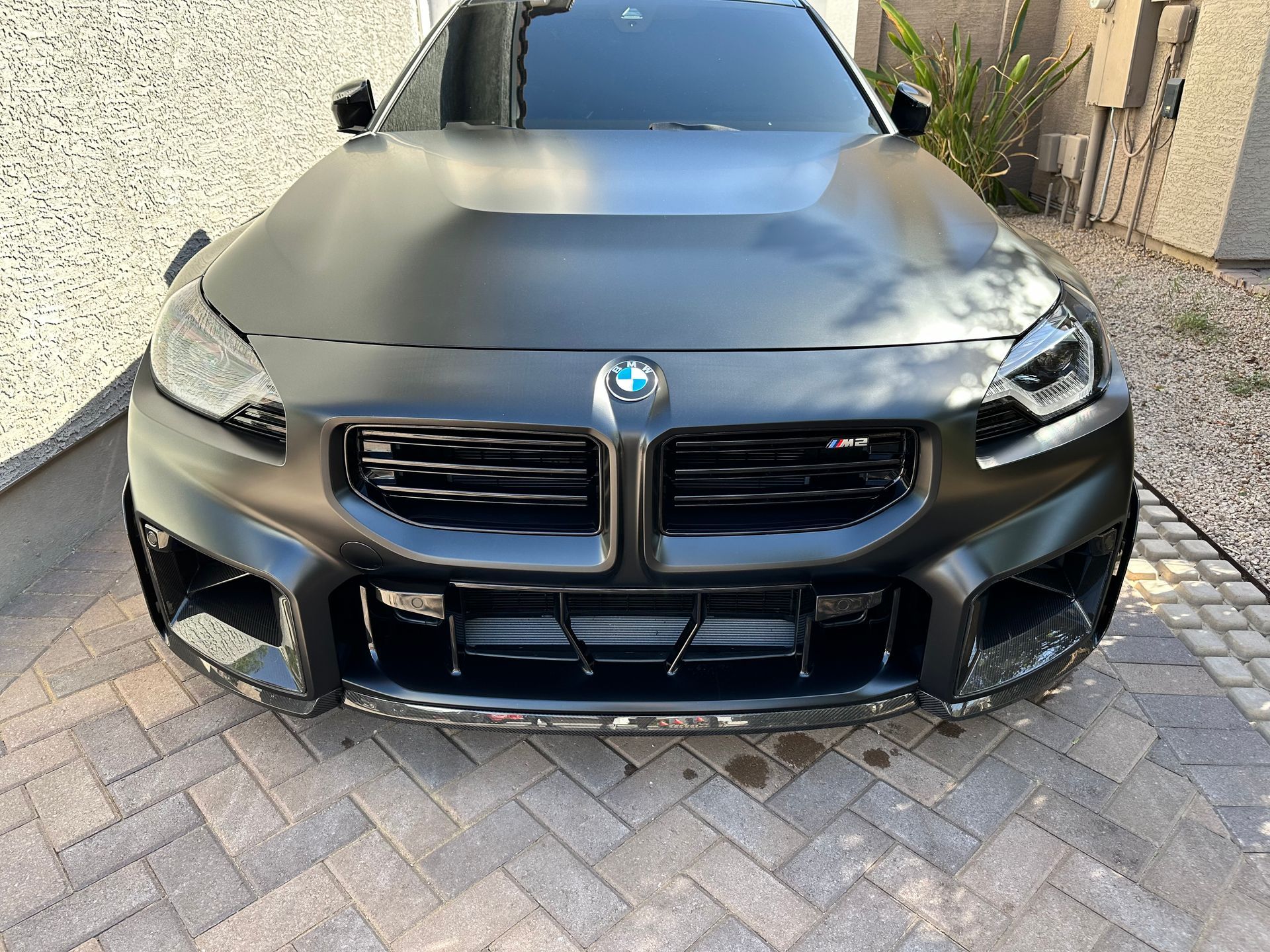A black bmw is parked on a brick driveway.