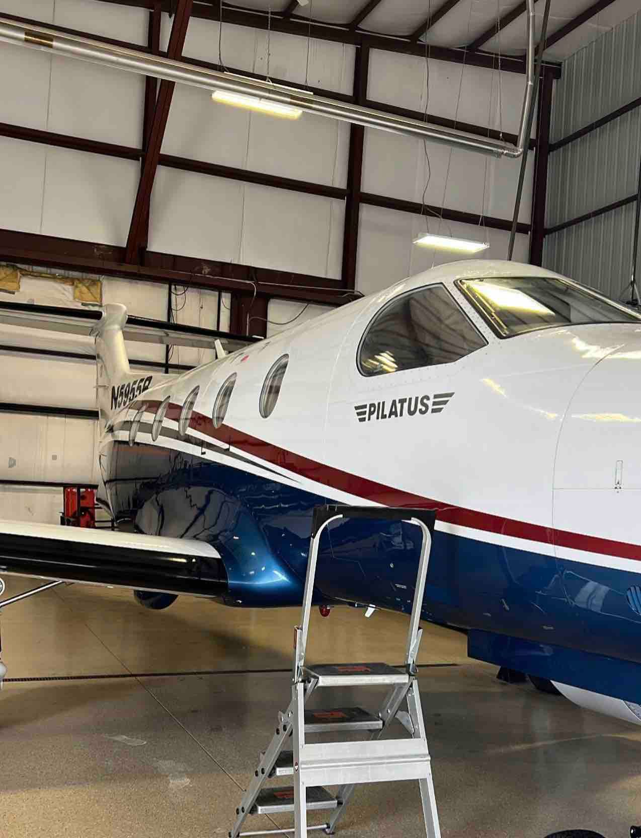 A blue and white plane is parked in a hangar with a ladder attached to it.