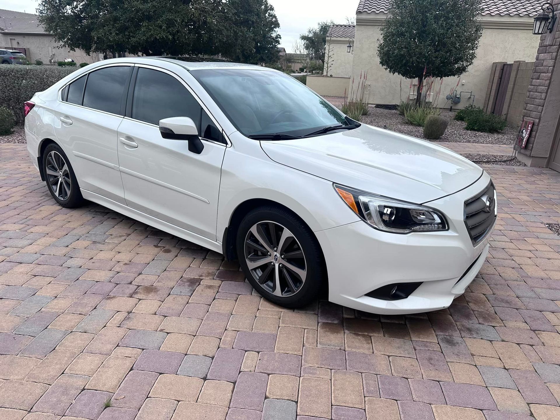 A white subaru legacy is parked on a brick driveway.