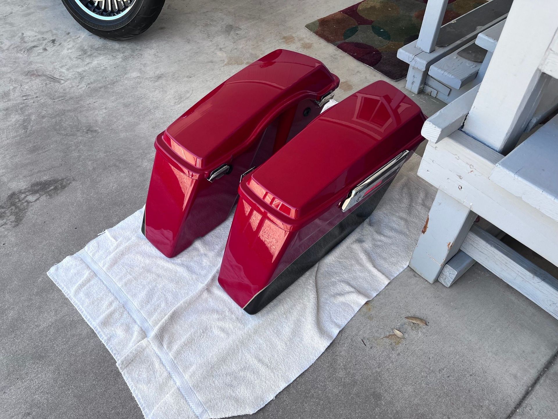 A pair of red motorcycle bags are sitting on a towel on the ground.
