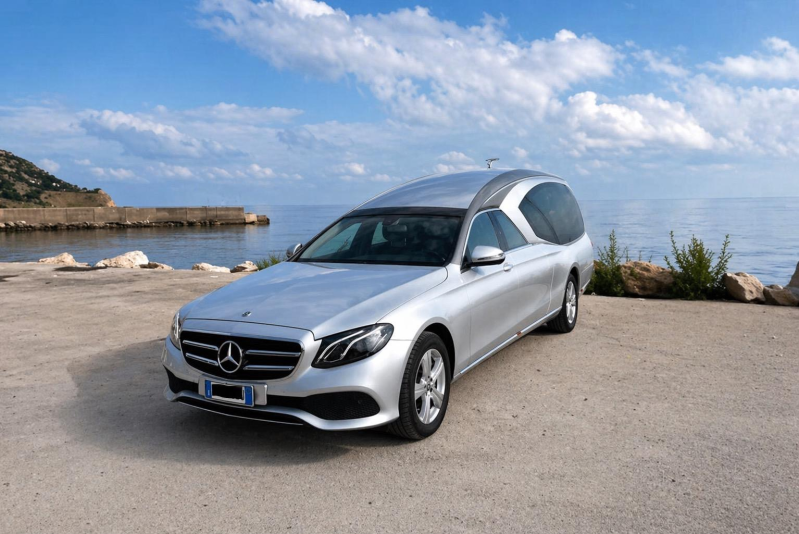 Una Mercedes-Benz argentata parcheggiata su una strada costiera sotto un cielo azzurro.