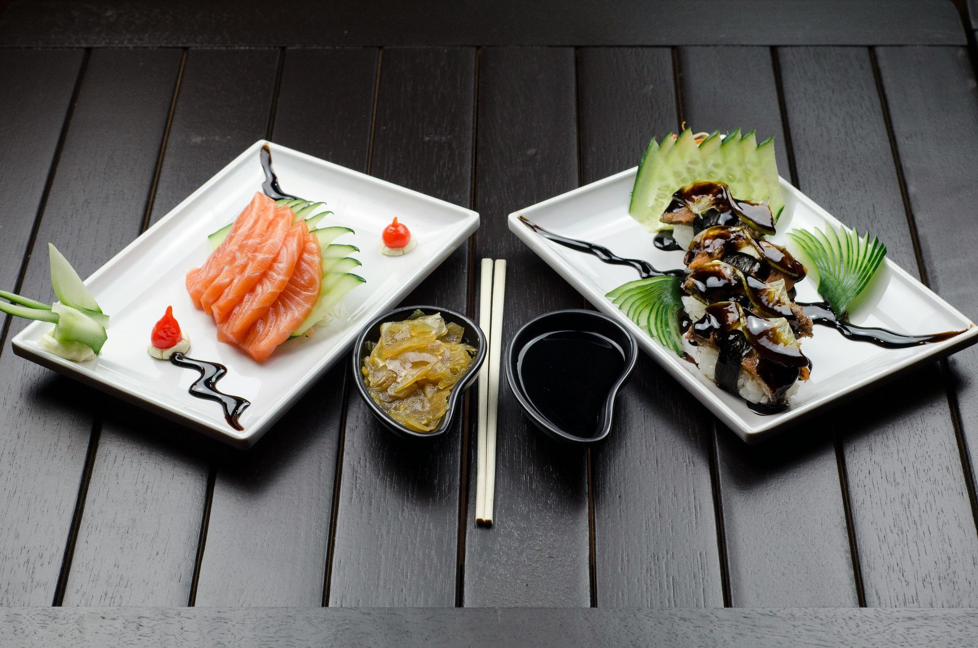Sushi and sashimi platter on a dark wood table. Salmon sashimi, sushi rolls, pickled ginger, and soy sauce are served.