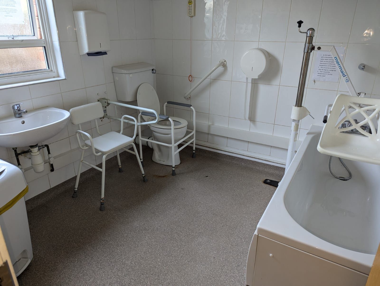 Accessible bathroom with sink, toilet, shower chair, and grab bars.