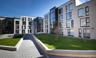 Modern apartment buildings with a paved courtyard, green lawns, and a central walkway.