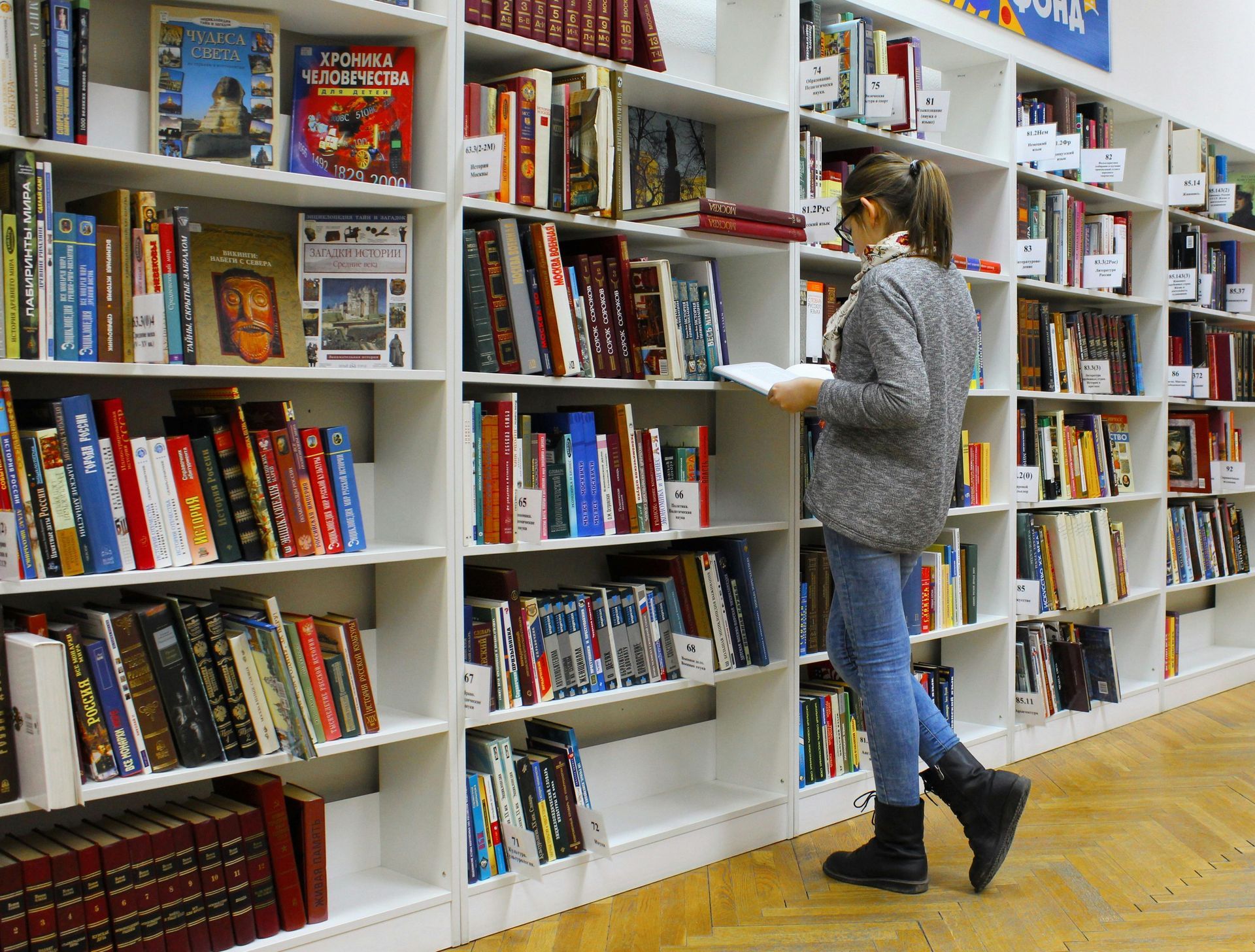 Student browsing books on a white library shelf