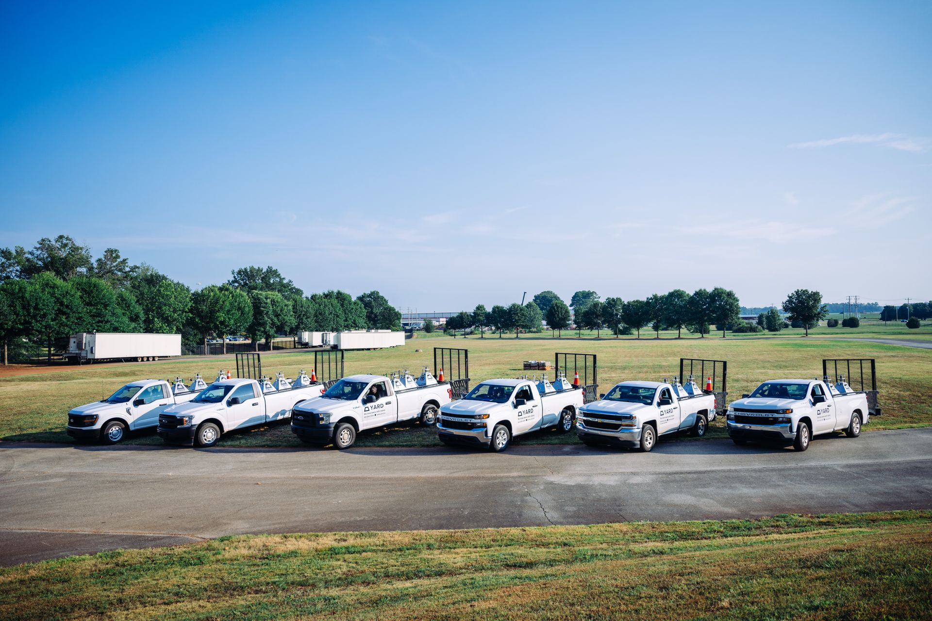 Six white utility trucks lined up on a gravel lot under a clear blue sky