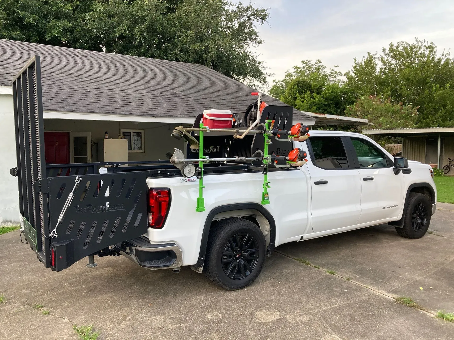 White pickup truck with camping gear secured in the bed, parked beside a house and trailer.