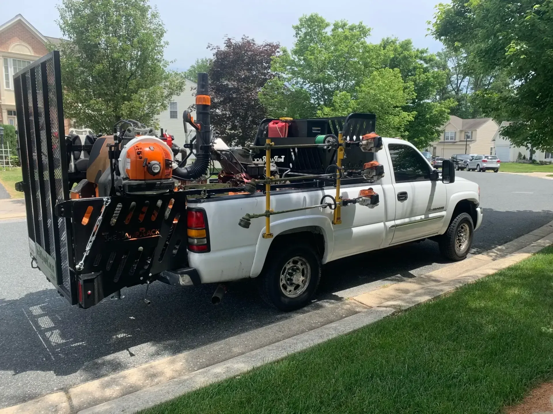 White pickup truck loaded with ladders, tools, and orange equipment parked by a suburban curb