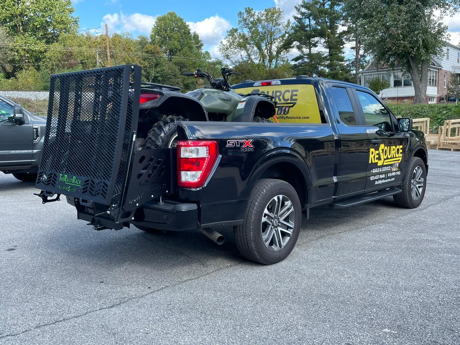Black pickup truck with open cargo rack and trailer attached, parked on a street near trees and houses.