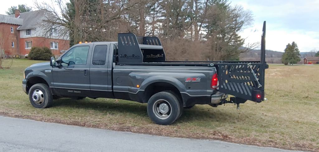 Black pickup truck with a rear crane and metal tailgate parked on a grassy roadside.