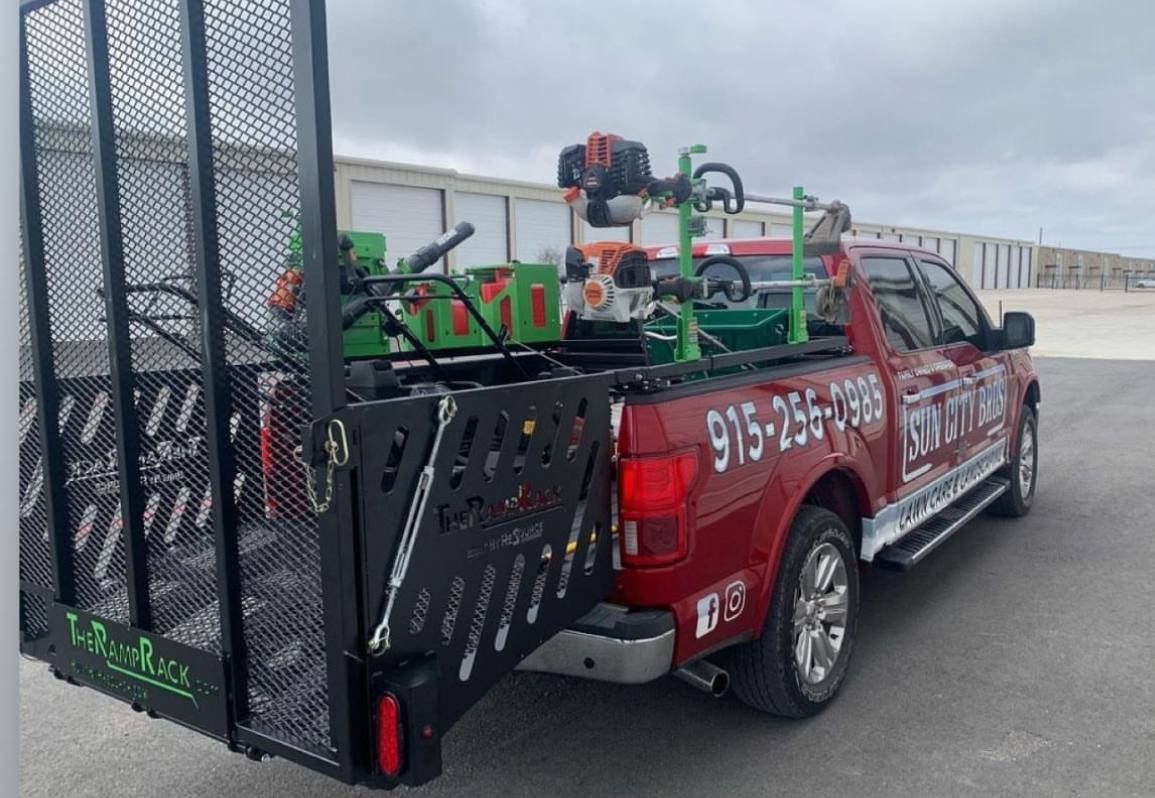 Red pickup truck towing green landscaping equipment on a trailer in a parking lot