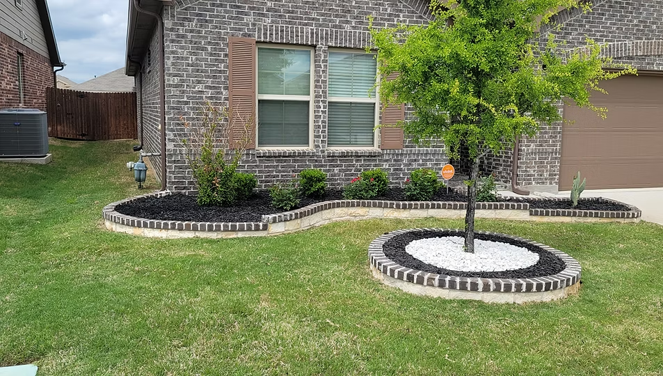 Brick house front yard with landscaped flower beds and a small tree on the lawn