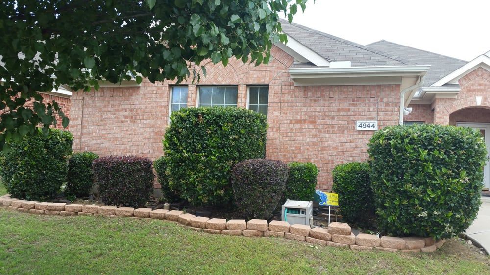 Brick house front yard with trimmed shrubs, stone border, and a mailbox by the walkway.