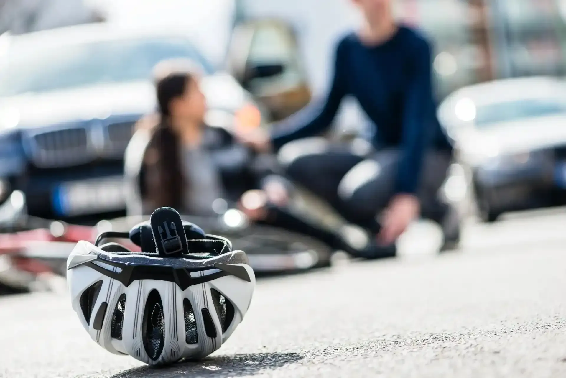 Casco da bicicletta sull'asfalto davanti a una persona ferita in un incidente in bicicletta, assistita da una persona interessata.