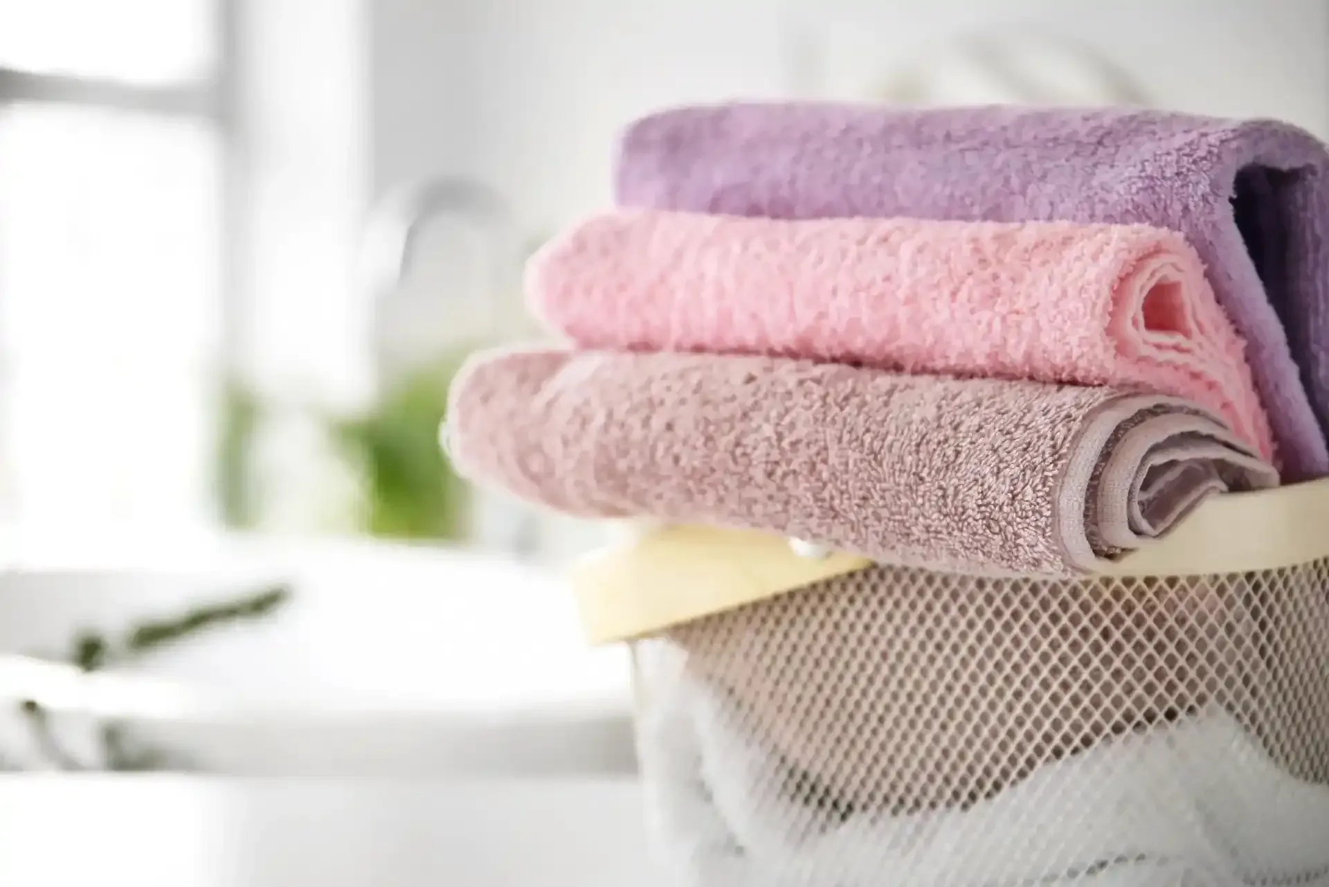 Pila di asciugamani color pastello piegati in un cesto a rete, sistemati in un bagno.