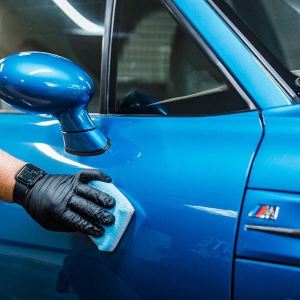 A gloved hand applies a blue detailing product to a bright blue car door.
