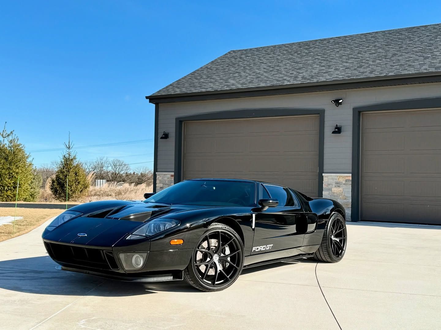 Black Ford GT sports car parked in front of a garage on a sunny day.