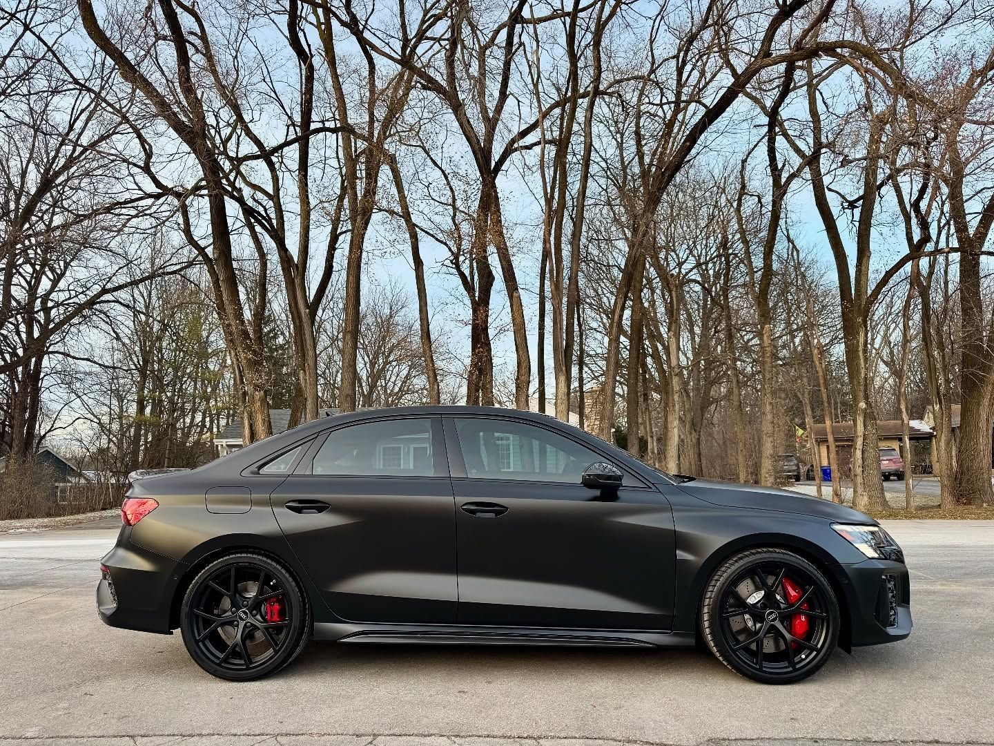Black Audi sedan parked on a road with trees in the background; red brake calipers visible.