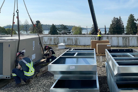 Workers installing HVAC unit on a rooftop with crane. Blue sky, lake in background.