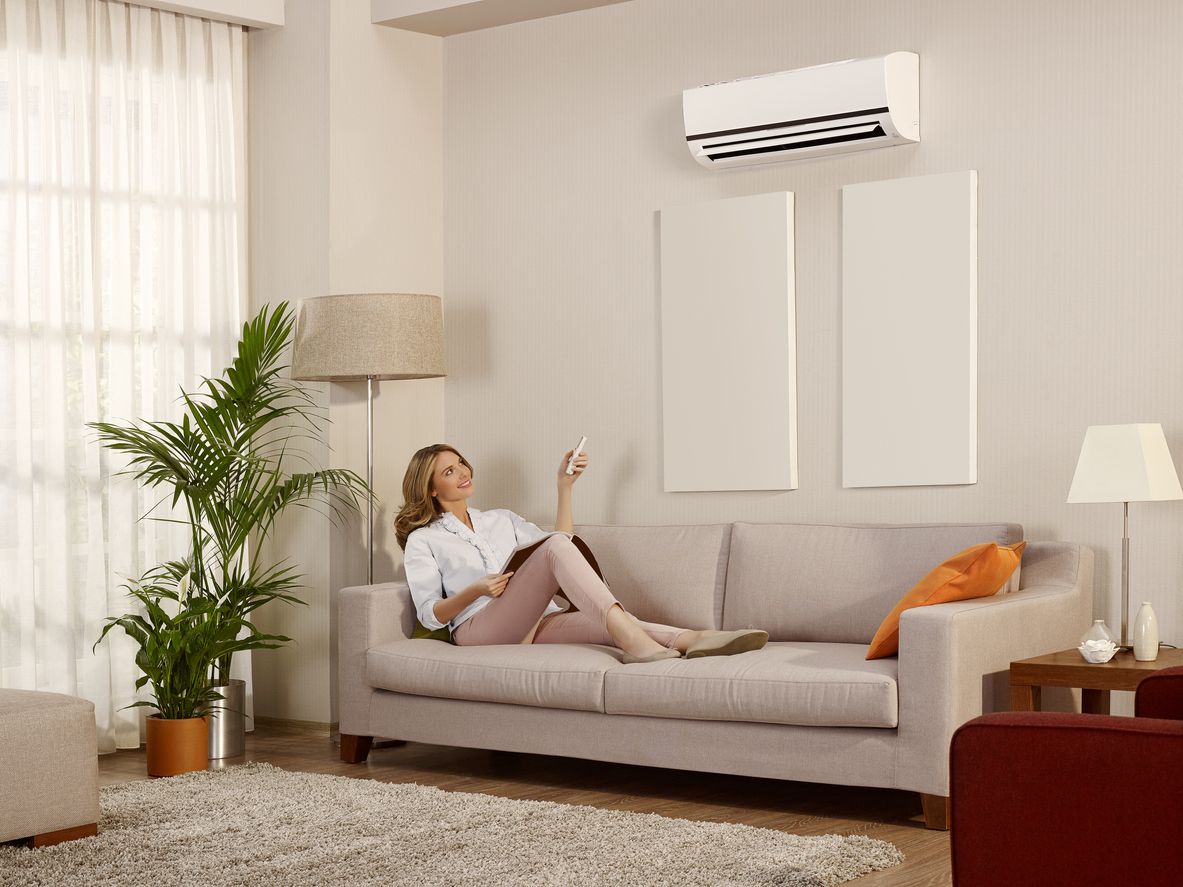 Air conditioner unit outside a brown house near a wooden deck and foliage.